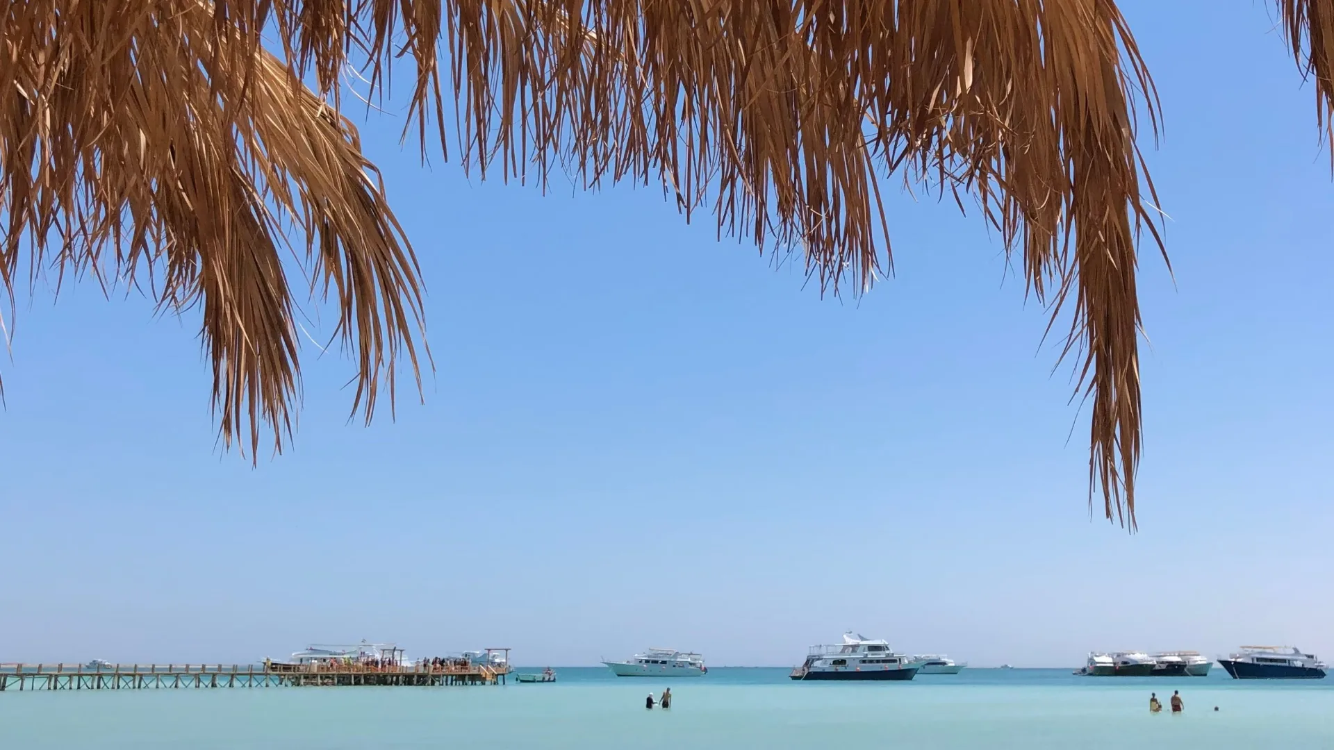 Blue sky over a sandy Red Sea beach with turquoise water, boats and a wooden pier